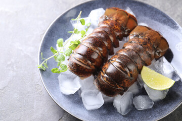 Raw lobster tails with microgreens, lime and ice on grey table, closeup