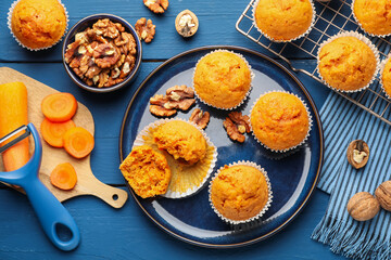 Tasty carrot muffins, walnuts and fresh vegetables on blue wooden table, flat lay