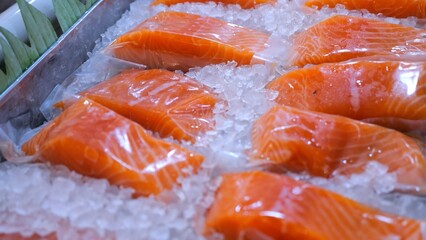 Fresh salmon fillets, individually wrapped in plastic, lay chilling on a bed of ice, ready for...