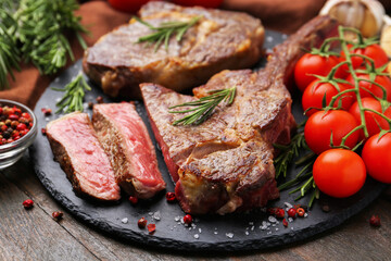 Pieces of delicious beef meat, spices and tomatoes on wooden table, closeup