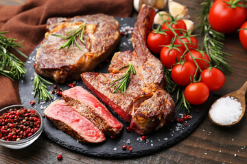 Pieces of delicious beef meat, spices and tomatoes on wooden table, closeup
