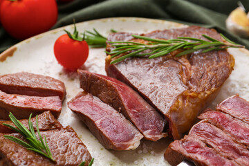 Pieces of delicious beef meat, spices and tomato on table, closeup