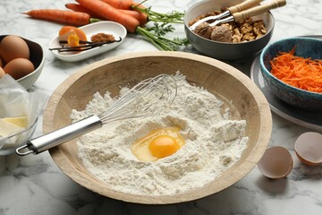 Making carrot cake. Bowl with flour, egg, whisk and other ingredients on white marble table, closeup