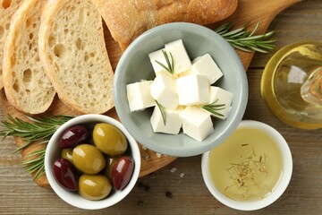 Delicious marinated olives, bread and feta cheese served on wooden table, flat lay