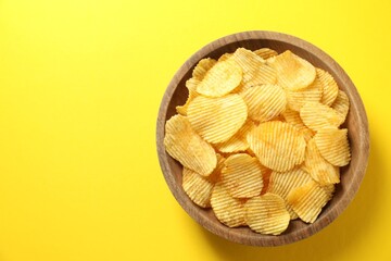 Tasty potato chips in bowl on yellow background, top view. Space for text