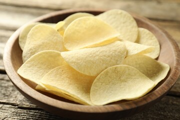 Tasty potato chips in bowl on wooden table, closeup