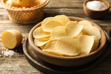 Tasty chips, salt and raw potatoes on wooden table, closeup