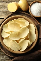 Tasty chips, salt and raw potatoes on wooden table, flat lay