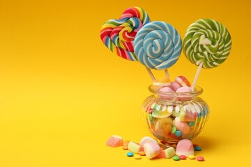 Different tasty candies in glass jar on yellow background. Space for text