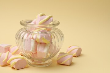 Tasty marshmallows in glass jar on beige background, closeup. Space for text