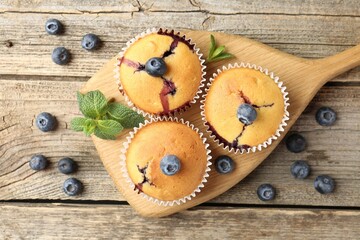 Delicious muffins with blueberries and mint on wooden table, flat lay