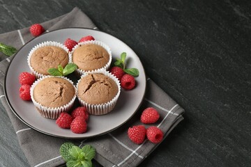 Delicious muffins with raspberries and mint on dark textured table, closeup. Space for text