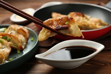 Dipping tasty fried gyoza (dumpling) into soy sauce on wooden table, closeup