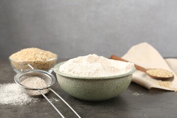 Brown rice, flour and sieve on grey table. Space for text