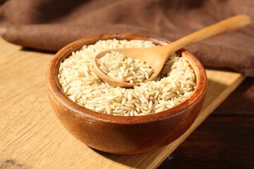 Brown rice and spoon in bowl on wooden table, closeup