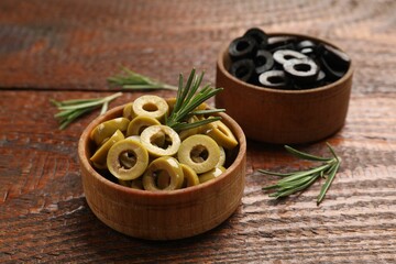 Different delicious marinated olive rings and rosemary on wooden table, closeup