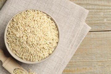 Raw brown rice in bowl and scoop on wooden table, top view. Space for text