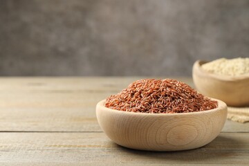 Raw brown rice in bowl on wooden table against grey background, closeup. Space for text