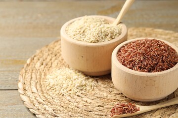 Different sorts of raw brown rice on wooden table, closeup