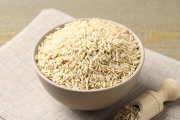 Raw brown rice in bowl and scoop on table, closeup