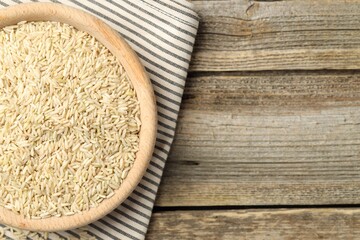 Brown rice in bowl on wooden table, top view. Space for text