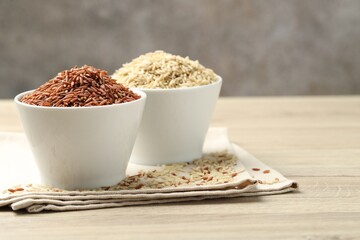 Different types of brown rice in bowls on wooden table, closeup. Space for text