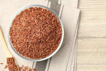 Brown rice in glass bowl and spoon on wooden table, flat lay. Space for text