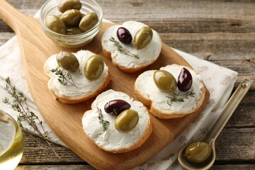 Delicious sandwiches with marinated olives, cream cheese and thyme on wooden table, above view