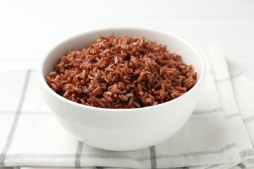 Tasty brown rice in bowl on white table, closeup