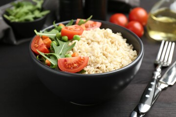 Delicious brown rice with vegetables on black wooden table, closeup