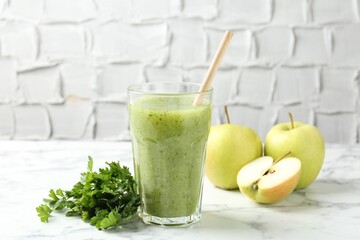 Healthy parsley smoothie in glass, leaves and apples on white marble table against grey textured background, closeup