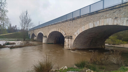 Fototapeta premium Crecida de río por abundantes lluvias atravesando antiguo puente de piedra en Burgos, España