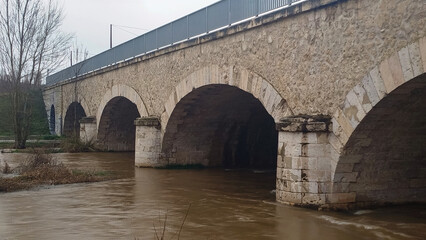 Crecida de río por abundantes lluvias atravesando antiguo puente de piedra en Burgos, España