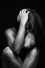 Sad lonely young woman crying while sitting on the floor in a dark room with an attitude of sadness and boredom with her legs together