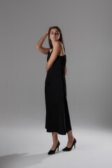Fototapeta premium Elegant woman in a black dress poses against a neutral background in a minimalist fashion setting