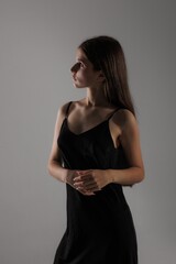 Fototapeta premium Young woman in black dress striking a thoughtful pose against a neutral background during a studio photoshoot
