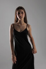 Naklejka premium Model poses confidently in a black dress against a simple gray backdrop during a fashion photoshoot