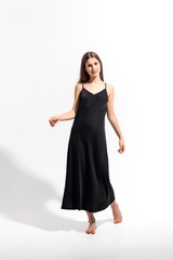 Elegant young woman poses in a black dress on a bright background in a stylish studio setting