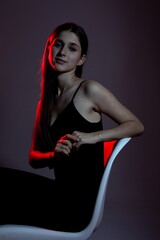 Young woman poses elegantly on chair with dramatic lighting in moody setting