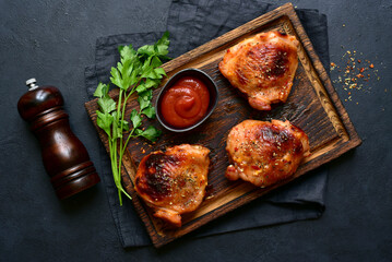 Roasted chicken thighs with ketchup on a rustic wooden board. Top view with copy space.