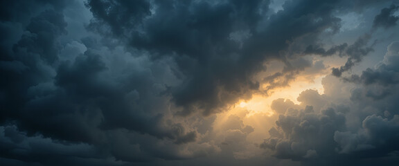 Obraz premium A dramatic sky filled with dark storm clouds, illuminated by a glowing golden light breaking through the cloud cover