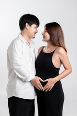 Pregnant woman and husband make a heart shape by placing their hands on their pregnant belly.