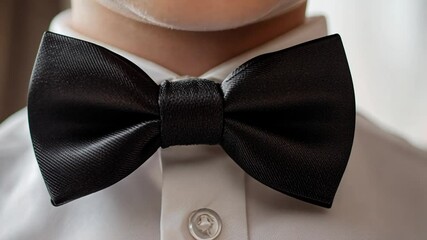 A close-up photograph of a young child wearing a formal white shirt and a black bow tie.