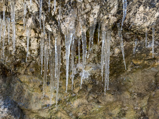 Obraz premium long transparent icicles hanging from a rocky cliff. frozen formations. spring thaw. rock texture. abstract background