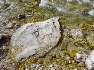 white rock in a shallow river with crystal clear transparent water and soft ripples. golden tones. assorted stone background. mountain