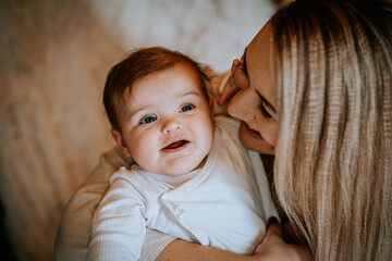 Smiling baby in mother’s arms, sharing a joyful and tender moment. The baby looks happy and engaged, capturing a loving family connection..