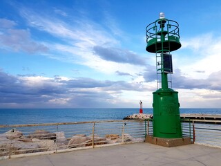 Green lighthouse on the seashore against the blue sky with clouds