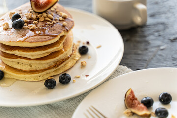Pancakes stacked with figs and blueberries on a white plate on a light gray background.