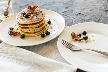 Pancakes stacked with figs and blueberries on a white plate on a light gray background.