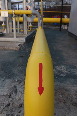 Bright yellow pipe with red arrow at industrial site — directional flow indicator in a technical...